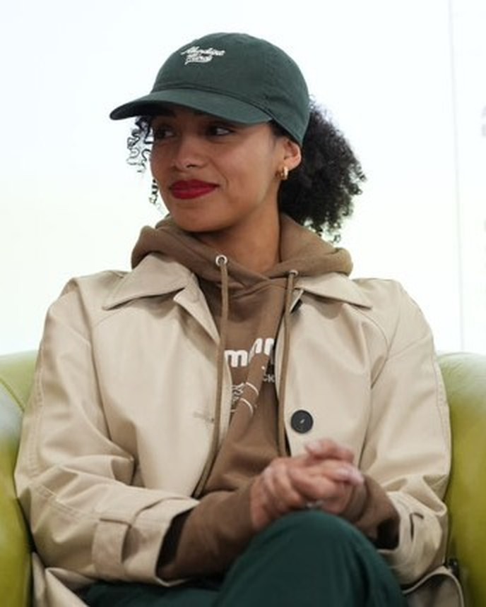 Tali Lama in a green cap and tan jacket, seated and smiling softly at an art exhibition and silent auction event